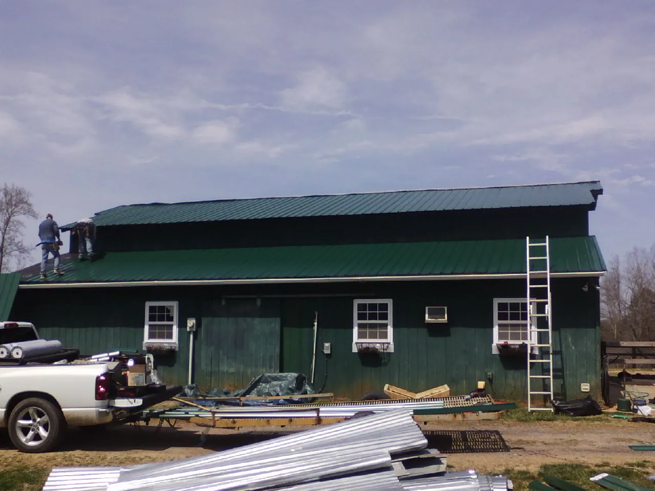 Crew installing green metal roofing on a large green barn in Grand Junction